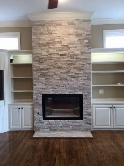 Floor-to-ceiling stacked-stone fireplace surround between white built-ins over a hardwood floor