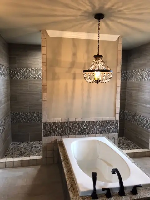 Drop-in tub in a tiled alcove with plank wall tile, a mosaic band and a beaded pendant light