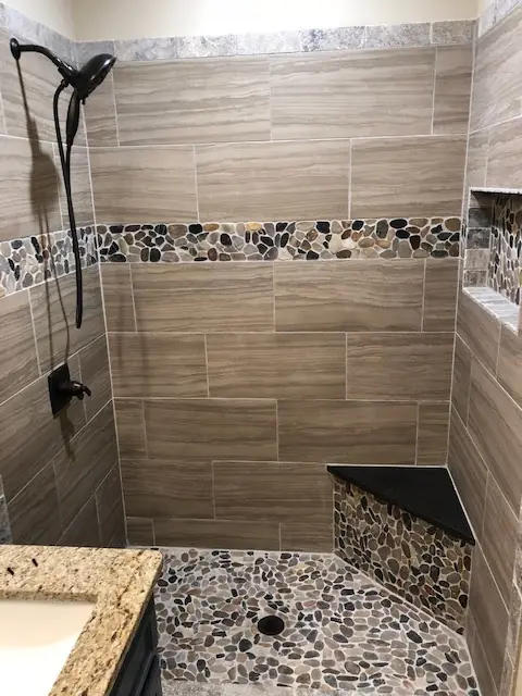 Finished walk-in shower with wood-look plank wall tile, a river-pebble band and a pebble floor