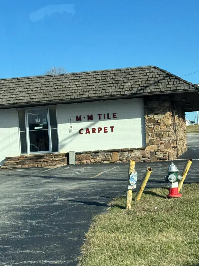 The M & M Tile & Carpet showroom, a low brick and stone building with red M M Tile Carpet lettering
